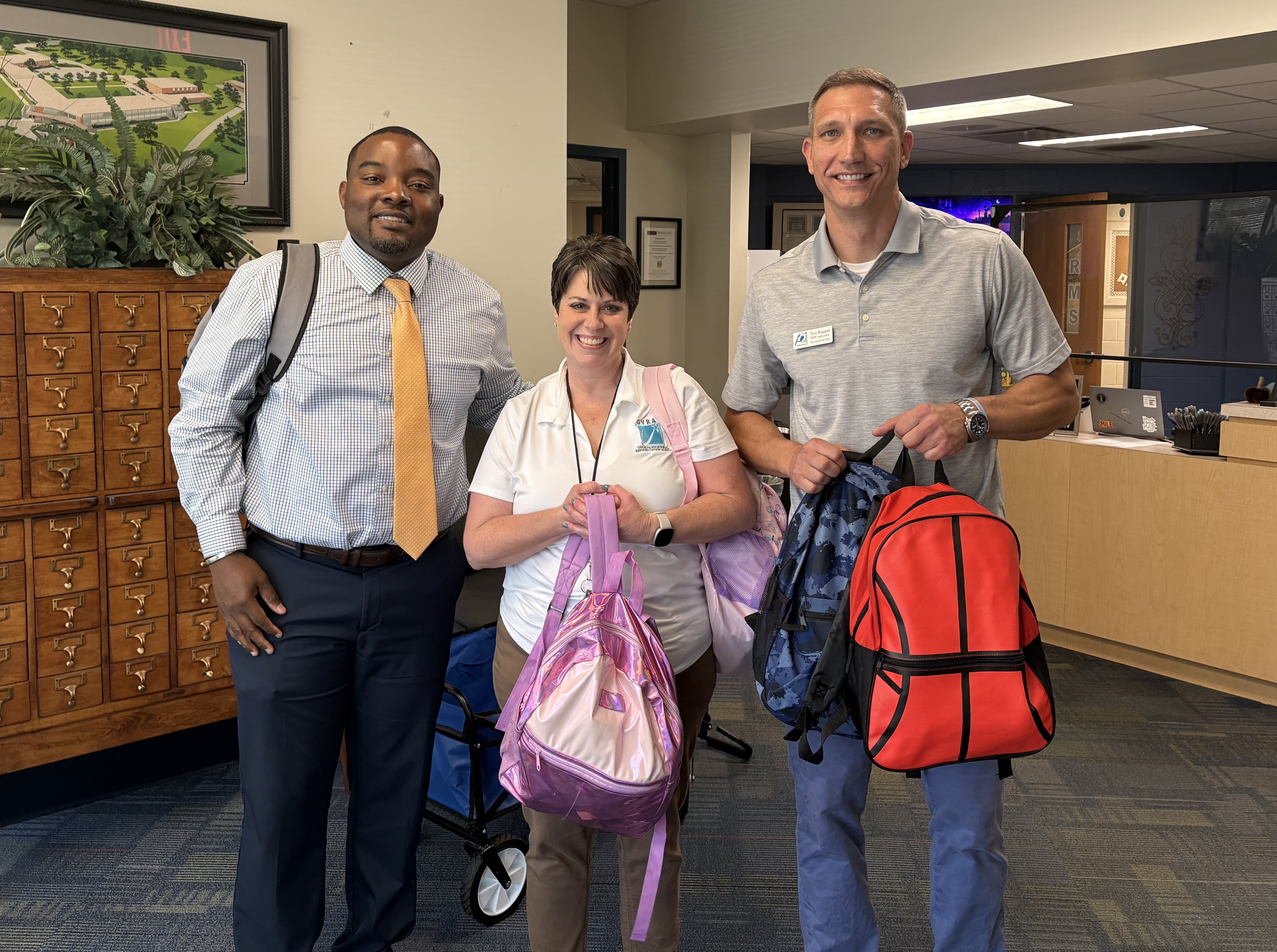 A man, a woman and another man standing in a lobby holding backpacks