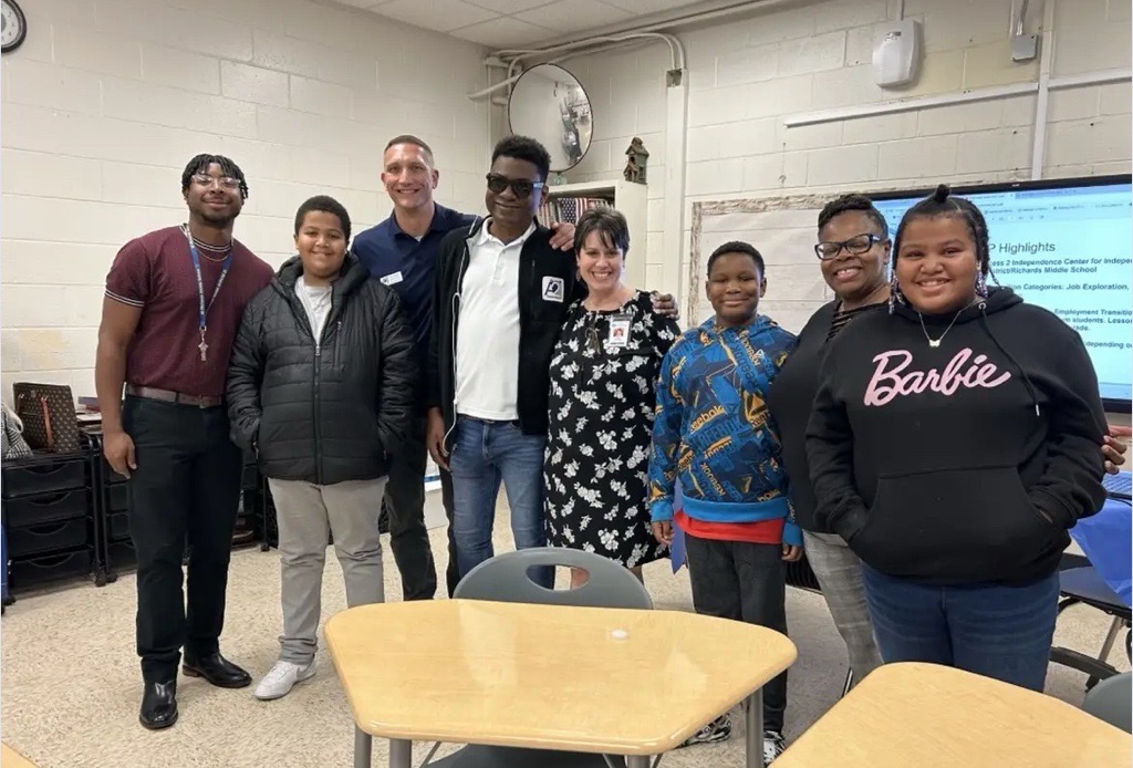 Group of students and adults standing in a classroom smiling.