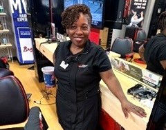 A woman holding a cup in one hand and is wearing a black apron. 