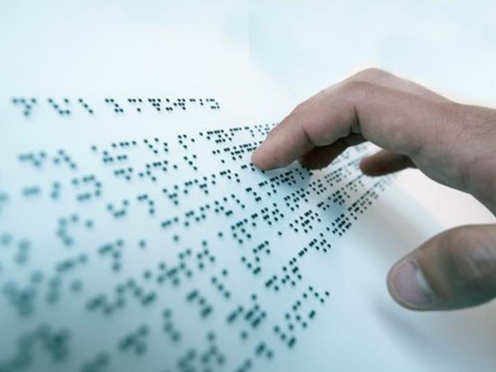 A person's hand reading Braille on Braille Paper