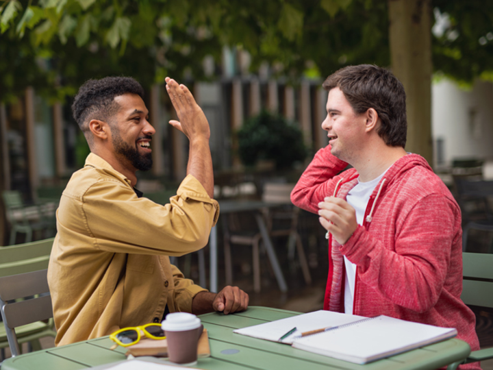 Two men hi-fiving in an outdoor cafe