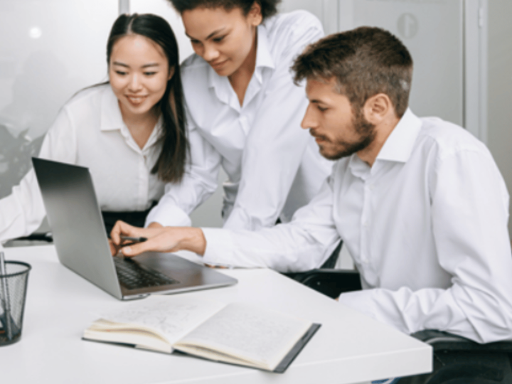 Three people that are wearing long sleeve white shirts are looking at the laptop. 