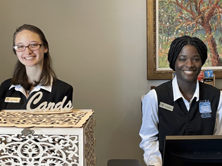 Two hospitality students smiling working on the front desk. 