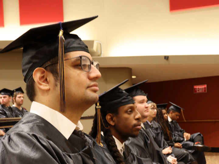 A group of graduates that are sitting down with their black cap and gown. 