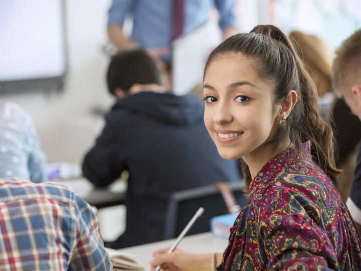 A girl in a classroom looking back in the classroom smiling. 