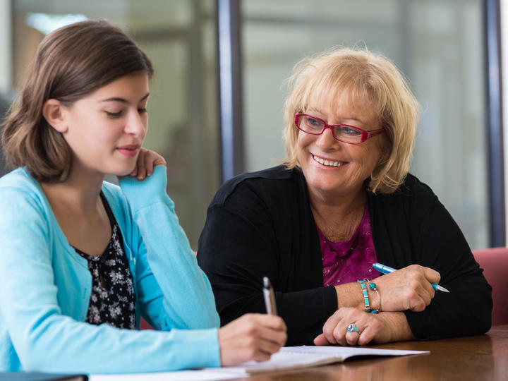An older lady and a student sitting together while the student is writing down information on a notepad. 
