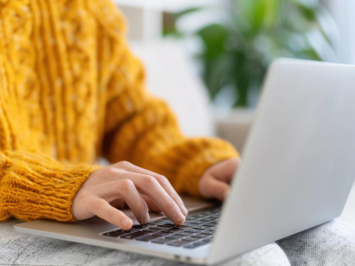 Person with a yellow sweater typing on the laptop. 