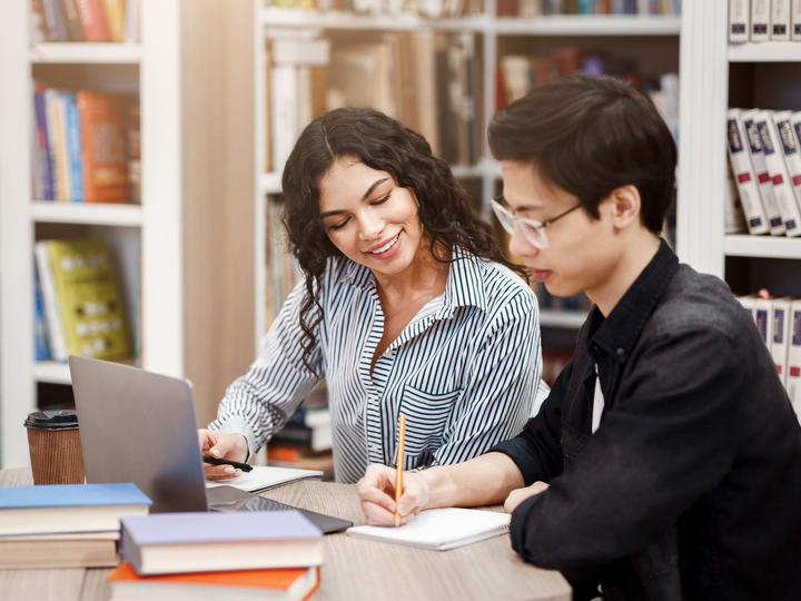 Two people in the library writing down information on their notepads. 