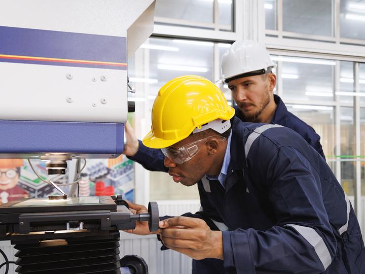 Two males with construction hats on looking through a microscope.