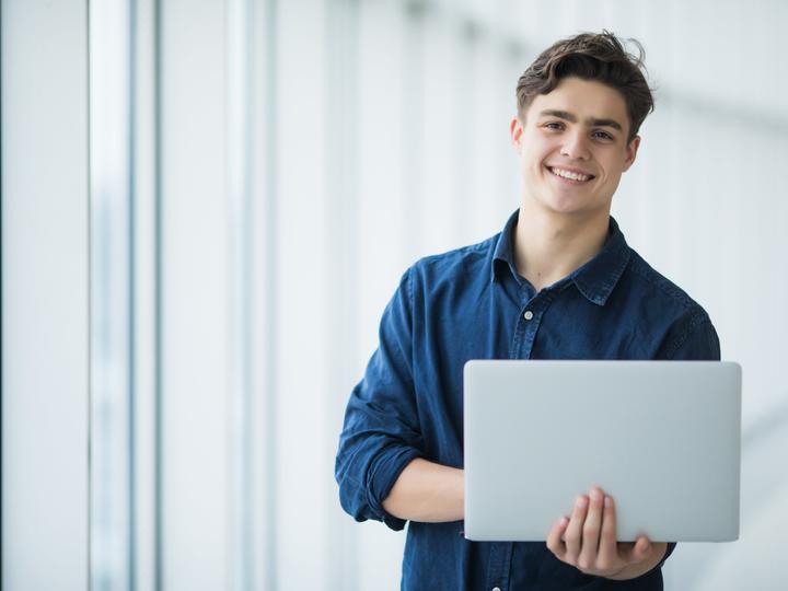 A photo of a Caucasian male who is holding his laptop in his hand. 
