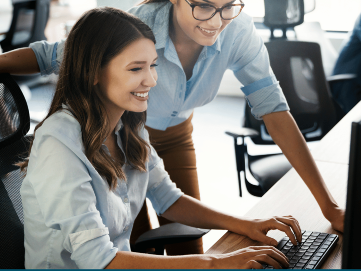 Two females smiling and looking at the laptop. 
