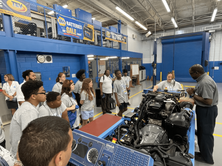A photo of an instructor showing a group students car parts. 