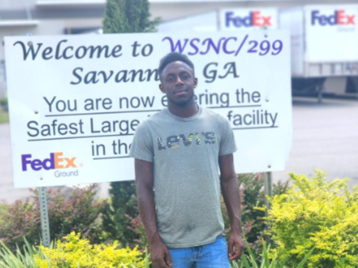 A man standing in front of a FedEx sign. 
