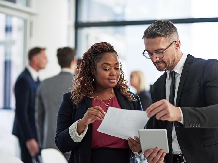 Two professionals dressed in suits and looking over a sheet of paper. 