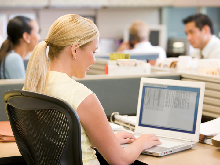 A photo of a female smiling and typing on her laptop. 