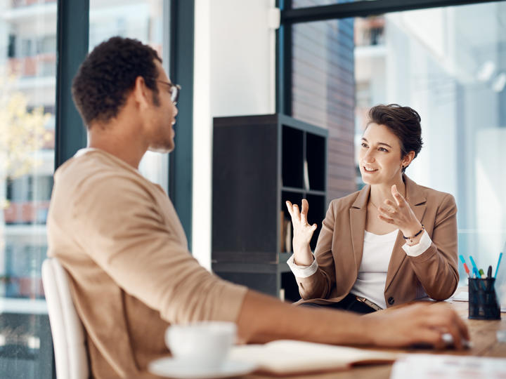 A woman and a man sitting down. The woman is holding her hands out and talking to the man.