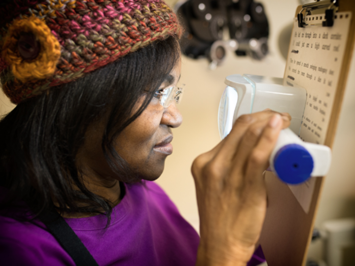 A person is holding a magnifier reading device in one hand and is looking through the device to see the words on a notepad. 
