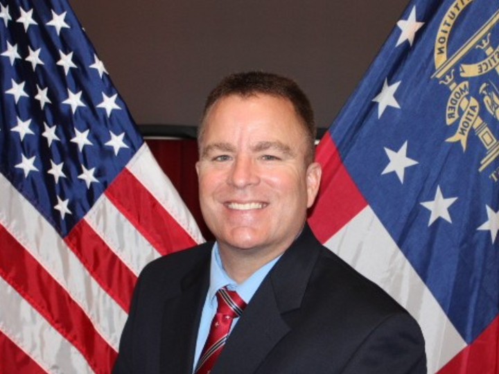 A man wearing a black suit standing behind flags. 