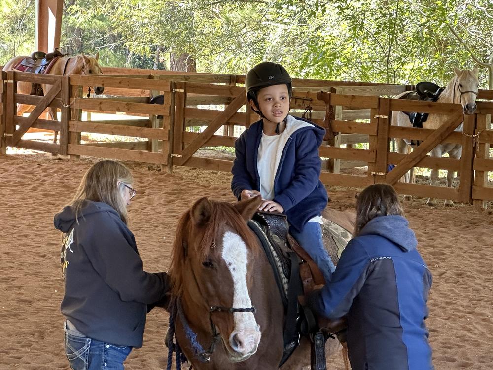 A young person on a horse with two adults on each side of the horse