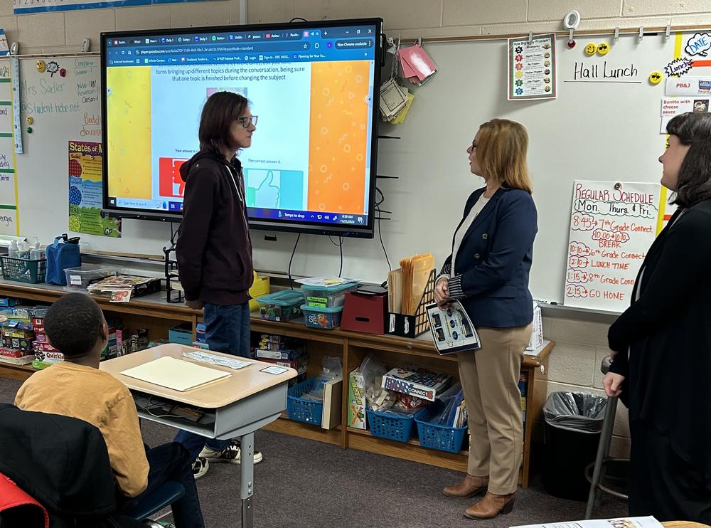 Male student facing a woman teacher in a classroom setting.