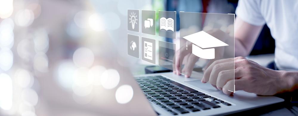 In the photo a person is typing on the laptop and there are educational icons surrounded over the laptop.
