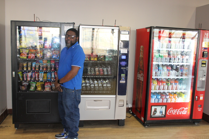 Stephen is standing by three vending machines. 