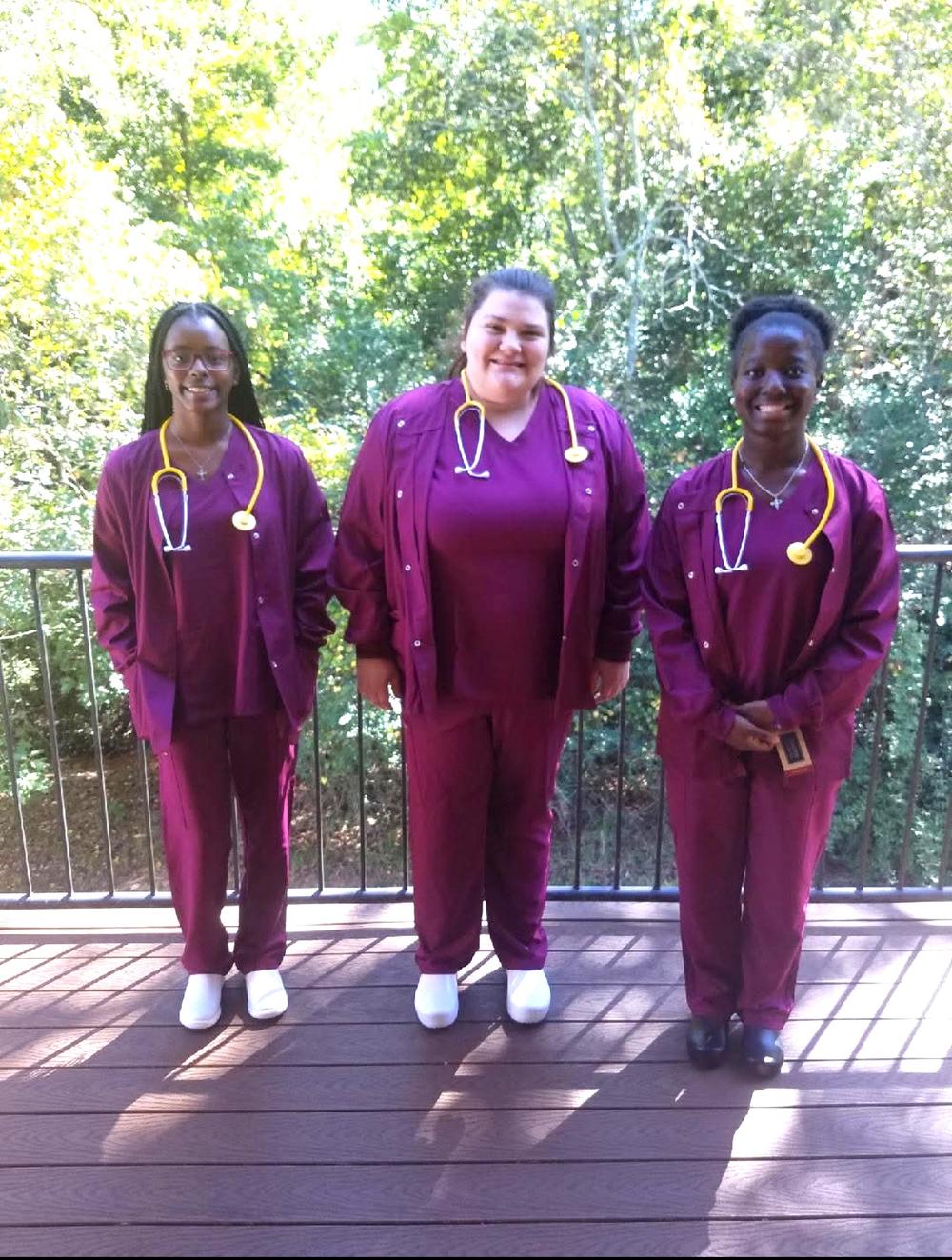 Three RWS nursing students wearing burgundy scrubs.