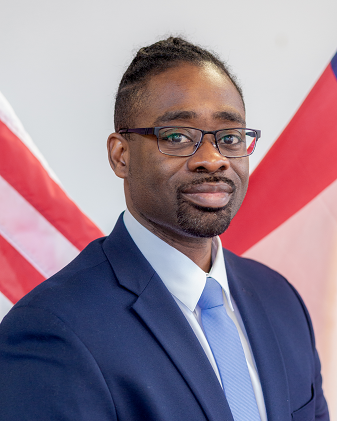 A headshot photo of Chris Wells wearing a dark blue suit and a light blue tie. 