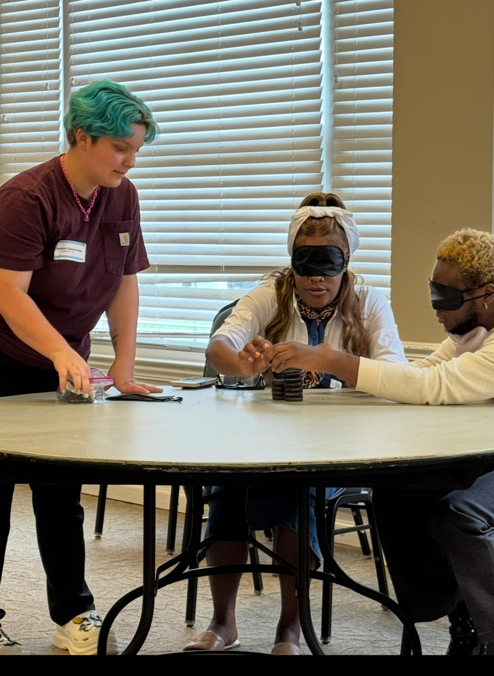 Two individuals blind folded sitting at a table participating in an activity with a facilitator