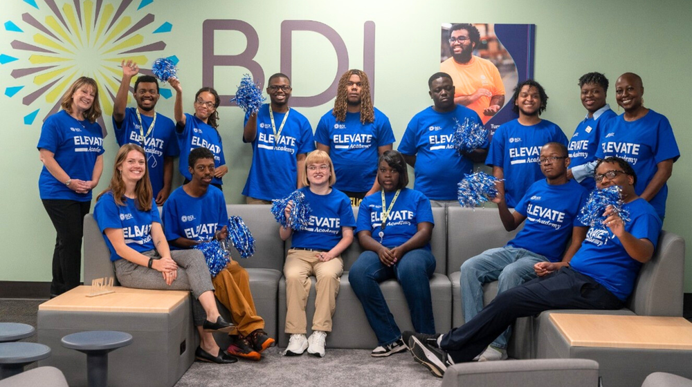 A group photo of students wearing blue shirts and have black and white pom poms in their hands.