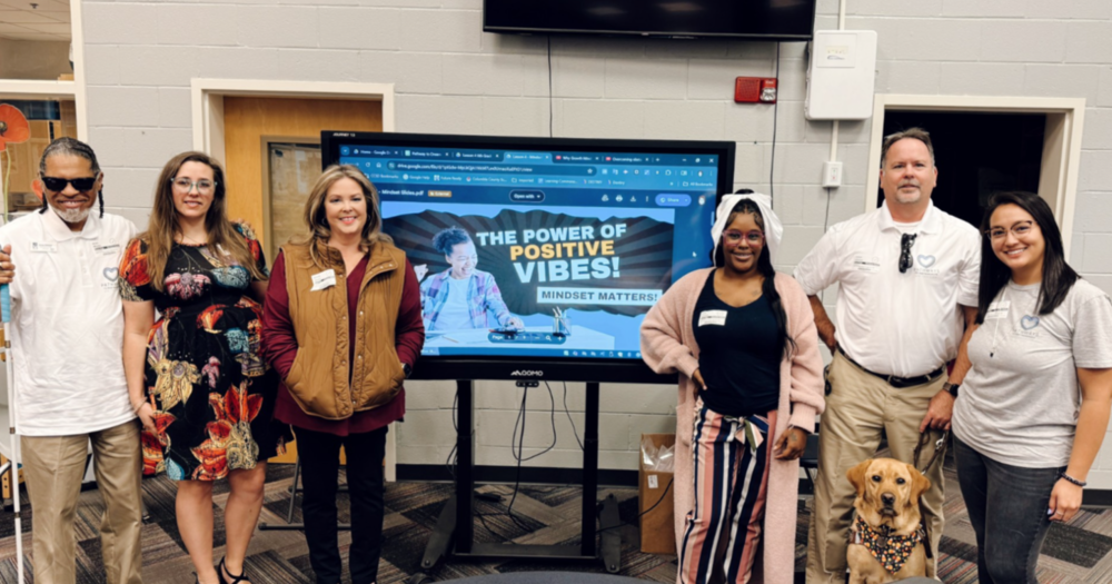 Group of adults: men, women and a dog taking a picture in front of a tv