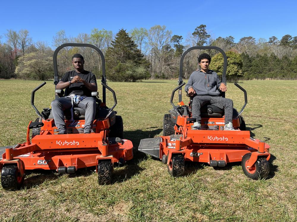 Two RWS students cutting grass on a red lawn mower. 