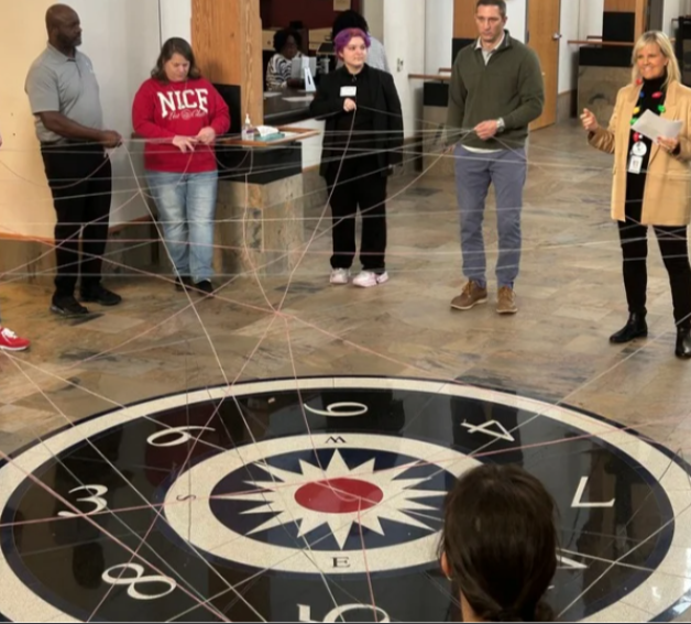 Individuals standing in a semi-circle, holding a piece of string. 