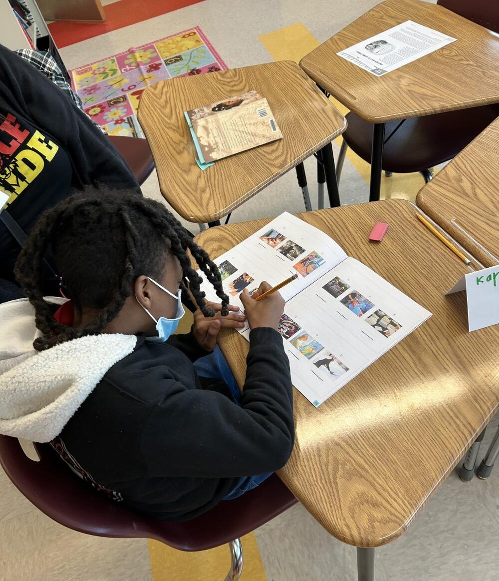 A student sits at a desk completing an activity in a workbook.