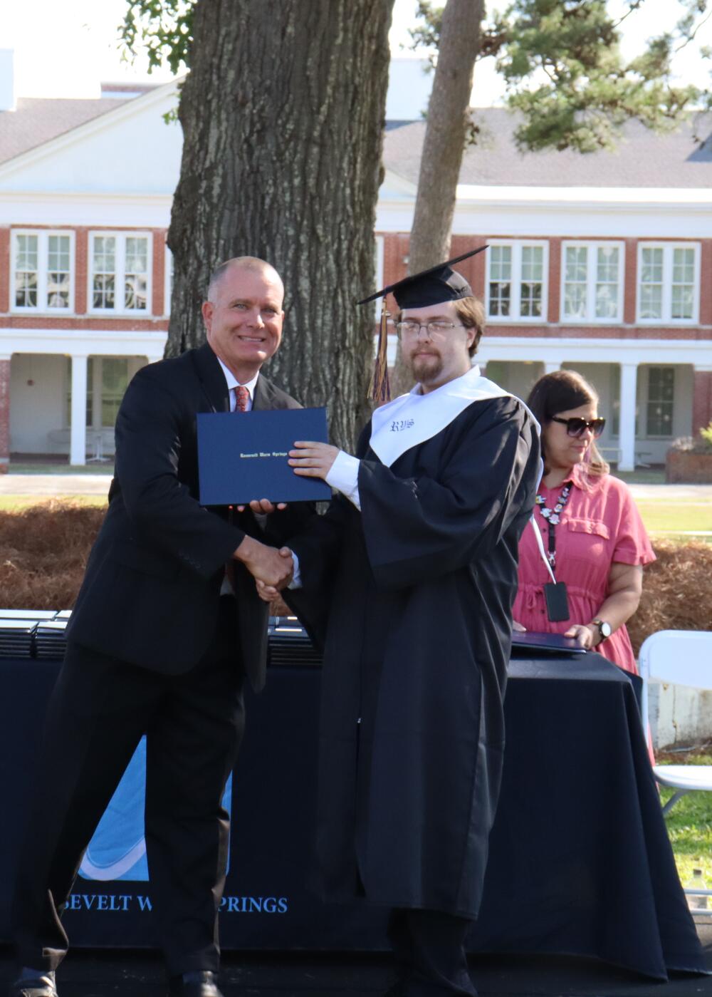 Two men shaking hands while one man is holding up his graduation certificate. 
