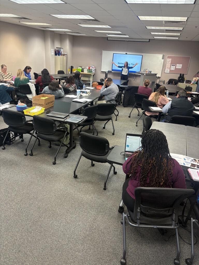 Room with people sitting at tables with a lead instructor. 