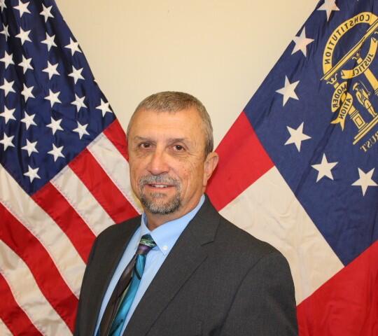 A man wearing a black suit standing behind two flags. 