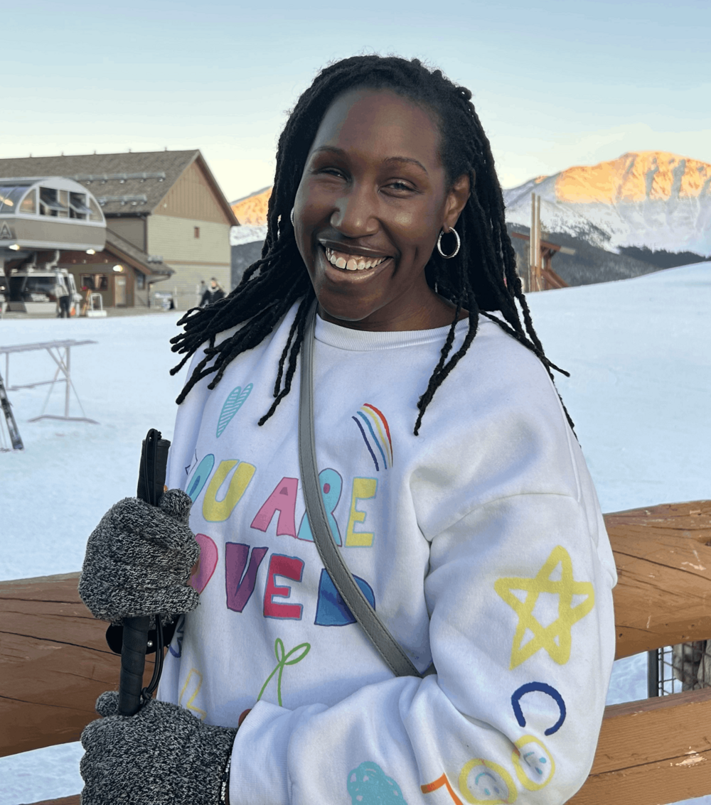 A woman smiling surrounded by snow behind her and is wearing a white sweater. 