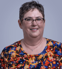 A woman wearing glasses with a short haircut smiling wearing a colorful blouse. 