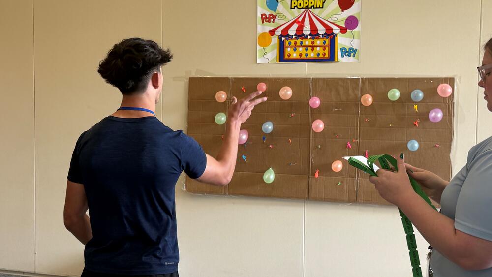 Student playing darts popping ballons. 