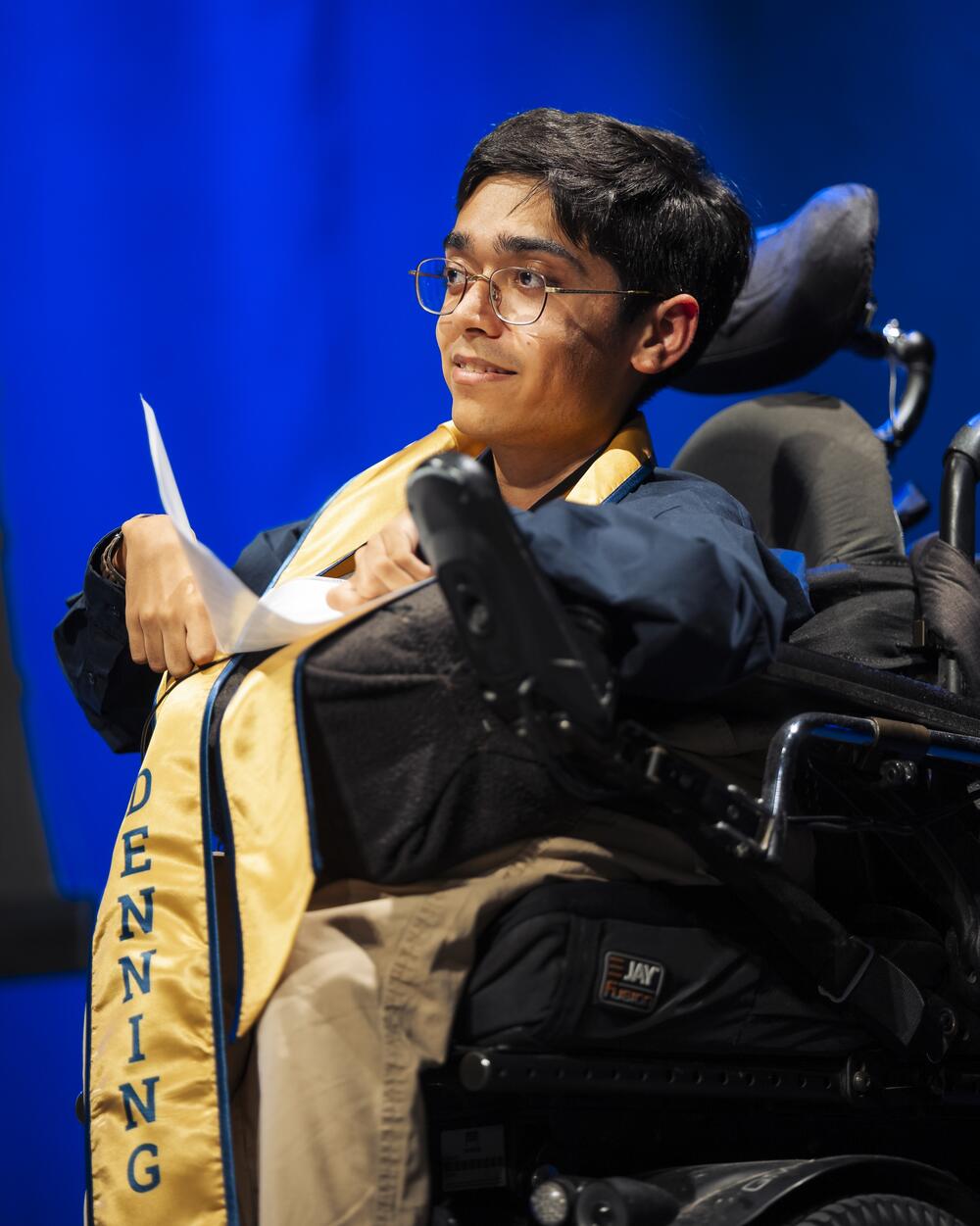 A man in a wheelchair is looking out in the distance while holding a piece paper in his hand. 