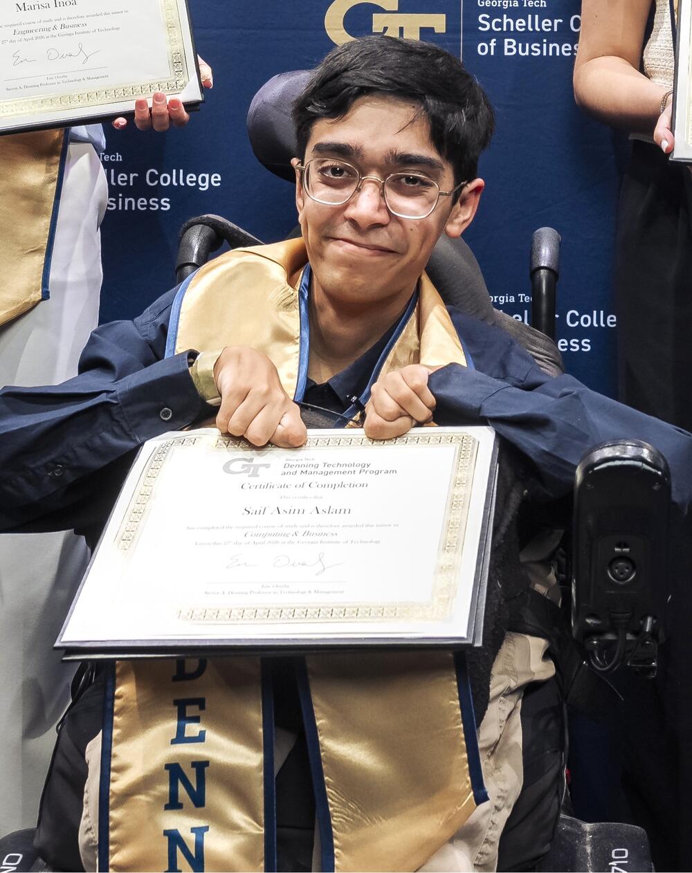 A man wearing glasses and a long sleeve navy blue short standing behind a Georgia Tech backdrop while holding up a certificate in his hands. 