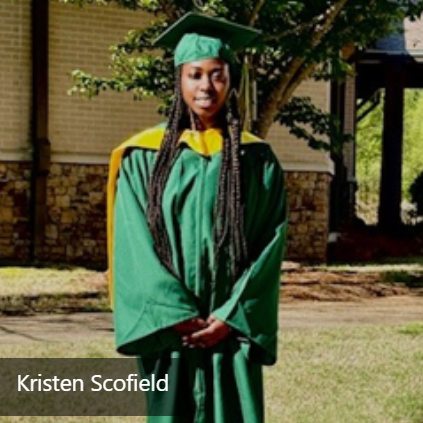  A woman wearing a dark green graduation cap and gown and standing behind a building and a tree. 
