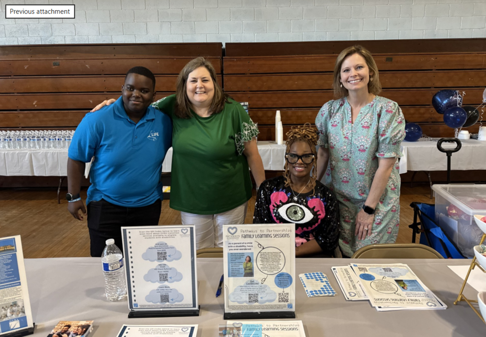 Group of 4 people; 1 male and 3 ladies standing behind a table with P2P information displayed