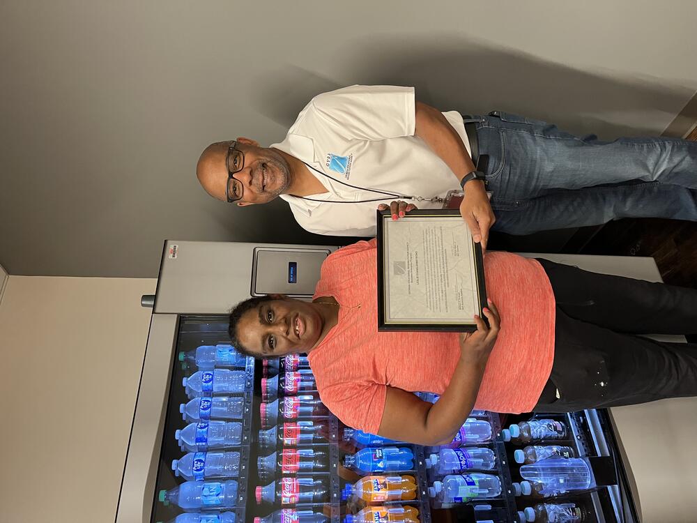 A woman wearing a pink shirt is standing right beside a man. They are both holding a certificate. 