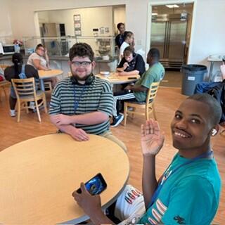 Two men sitting down at a table and one of them is waving their hands. 