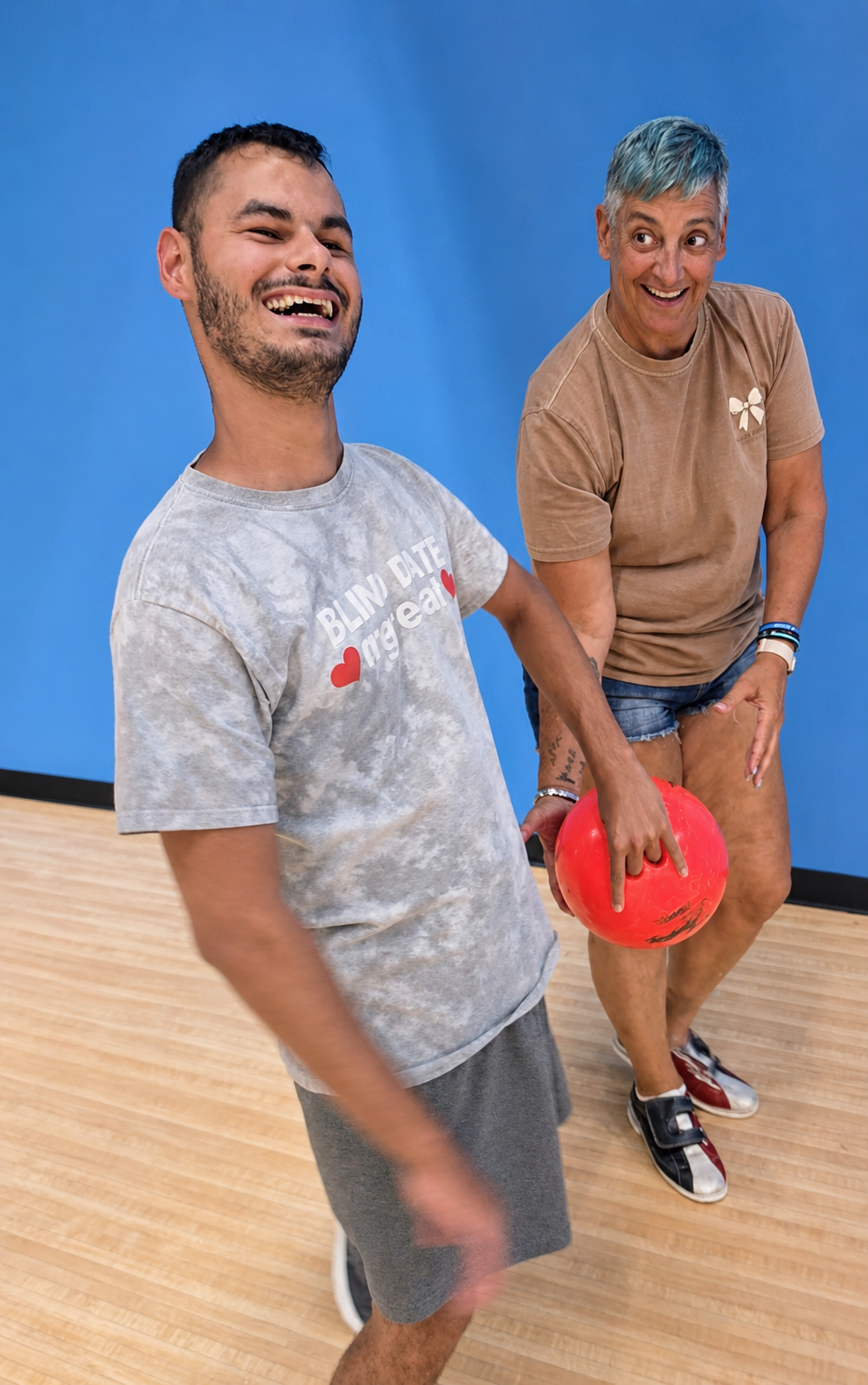 Two men standing beside each other laughing and one of the men is holding a red ball. 