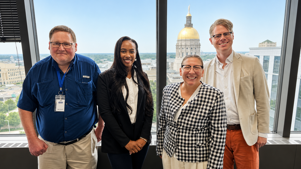 Four people standing behind a window has the capitol building in the background. 