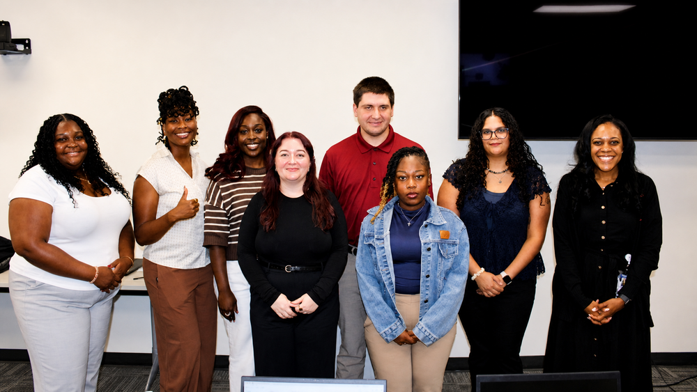 A group of professionals standing behind a white wall and a flat screen T.V. 