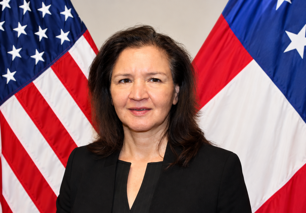 A woman wearing all black and standing behind two flags. 